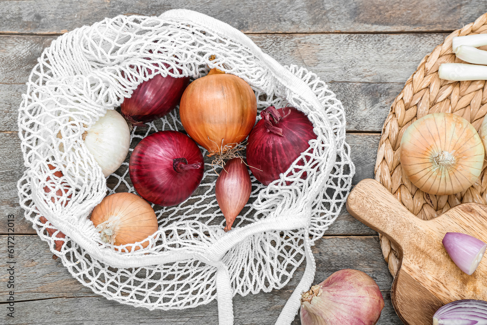 Board and string bag with different kinds of onion on brown wooden background