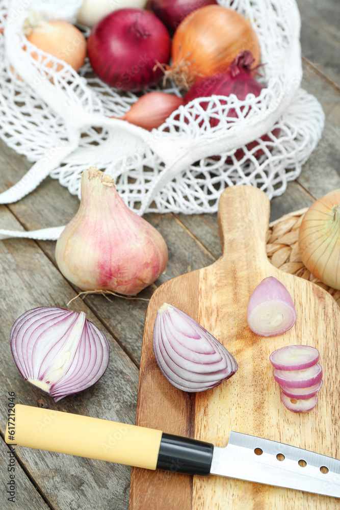 Board and string bag with different kinds of onion on brown wooden background