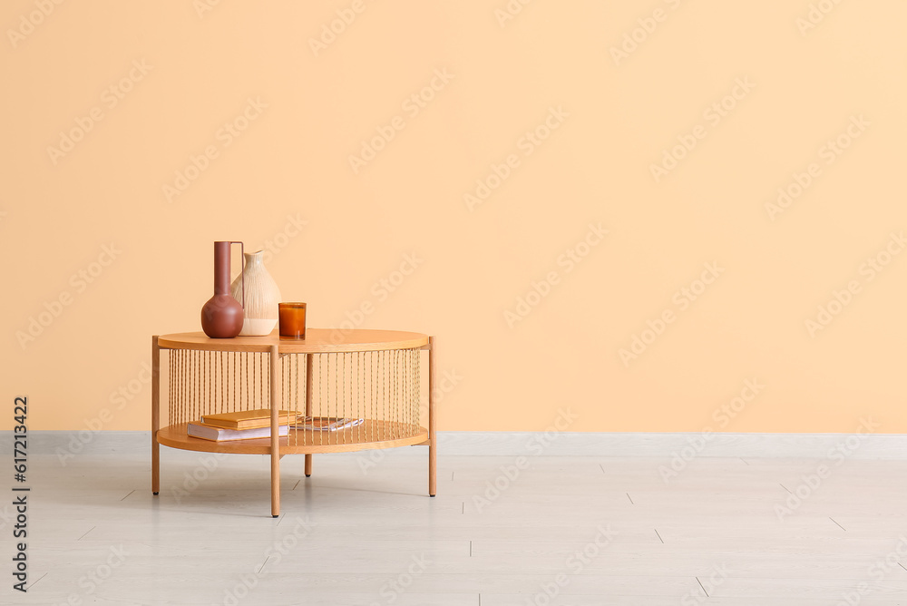 Wooden coffee table with empty vases, candle, books and magazine near beige wall