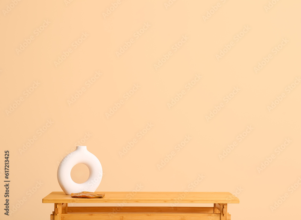 Wooden table with empty vase near beige wall