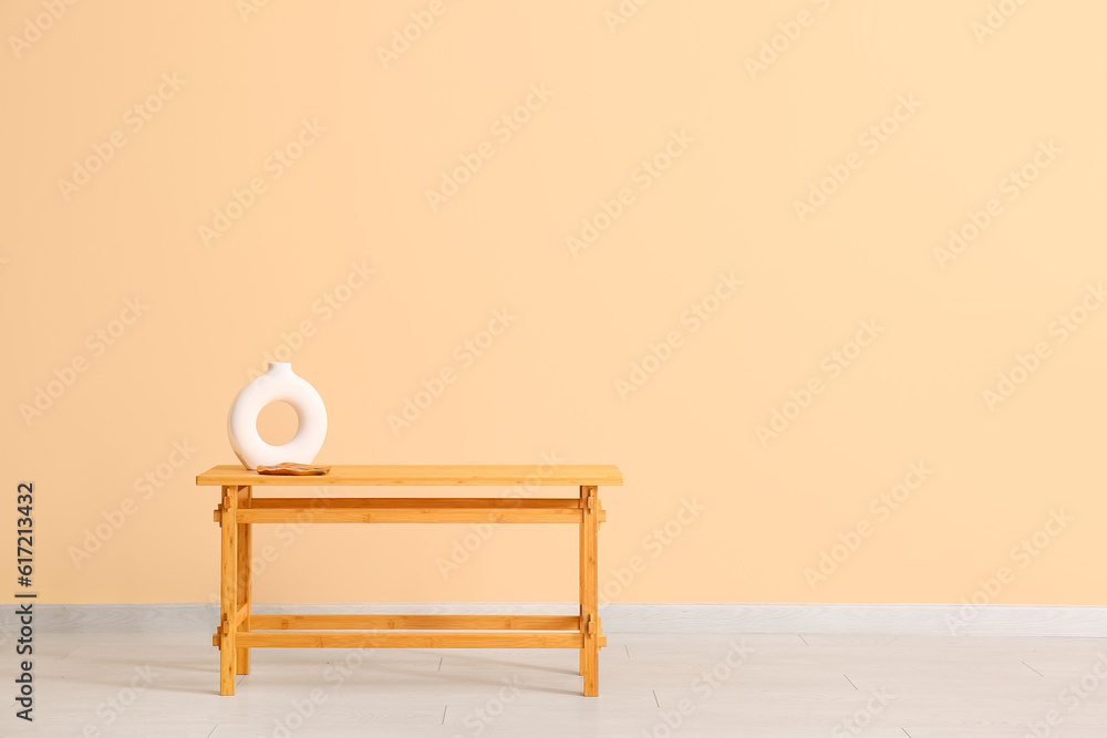 Wooden table with empty vase near beige wall