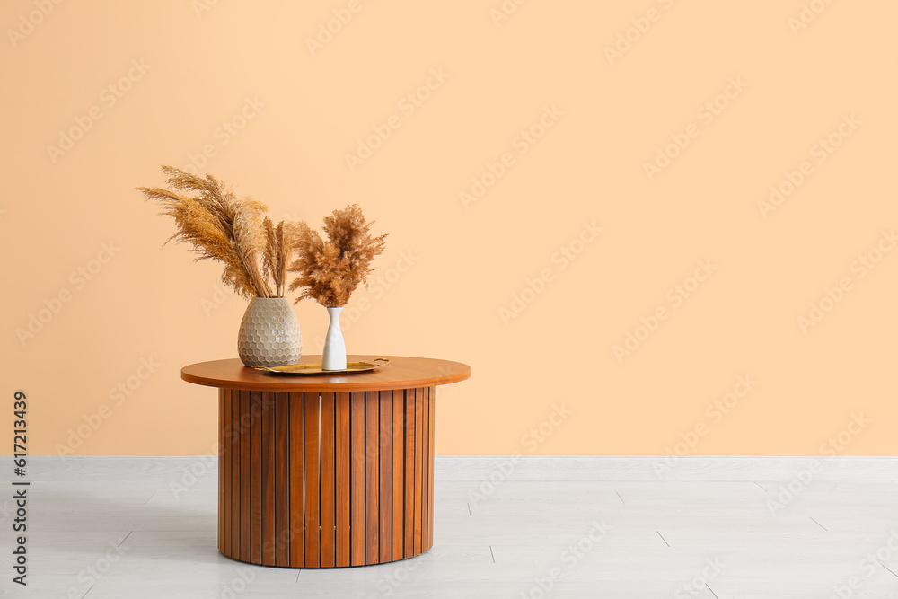 Vases with pampas grass on wooden coffee table near beige wall