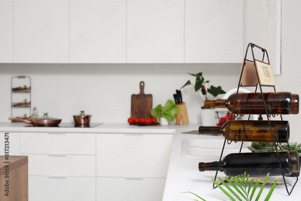 Rack with wine bottles on white countertop in modern kitchen