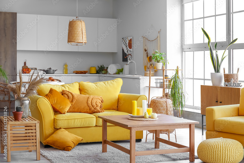 Interior of light open space kitchen with yellow sofa, armchair and wooden coffee table