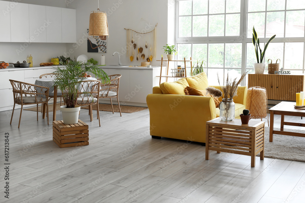 Interior of light open space kitchen with yellow sofa and houseplant on wooden box