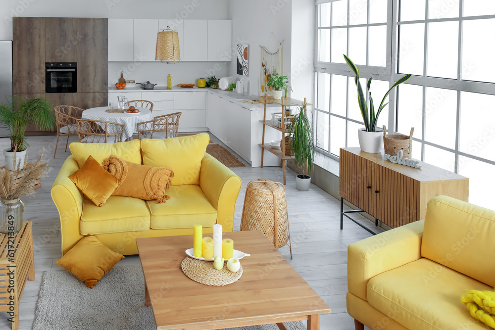 Interior of light open space kitchen with yellow sofa, armchair and wooden coffee table