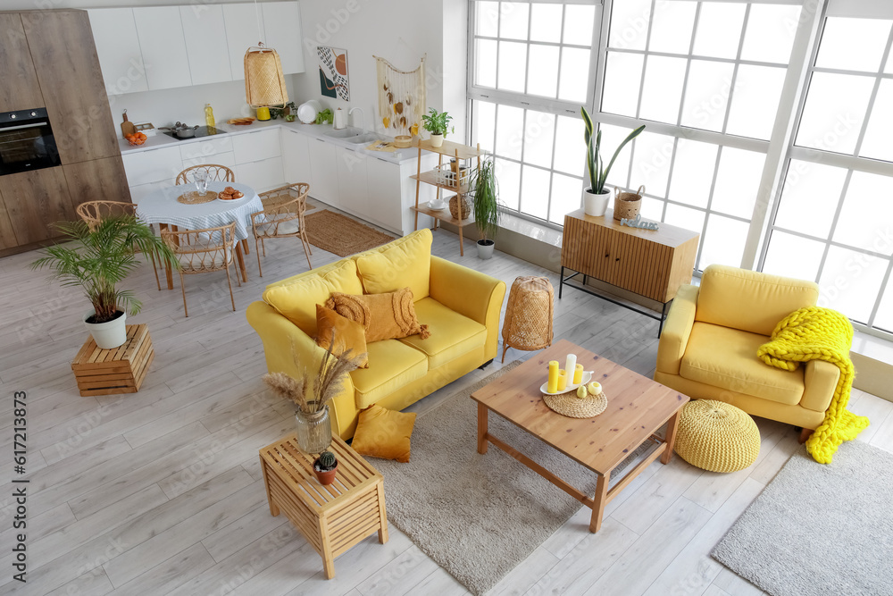 Interior of light open space kitchen with yellow sofa, armchair and wooden coffee table