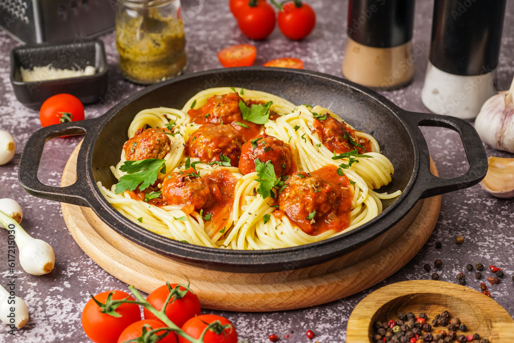 Frying pan of boiled pasta with tomato sauce and meat balls on grey table