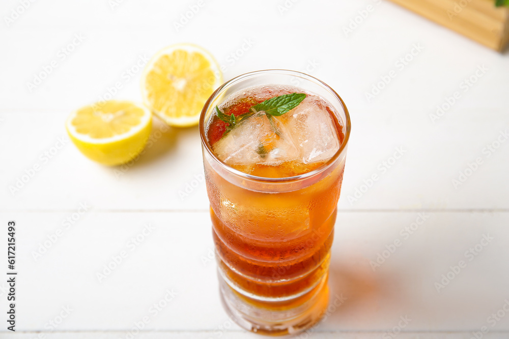 Glass of ice tea with mint and lemon on white wooden background