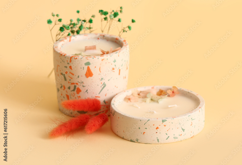 Holders with candles and flowers on beige background