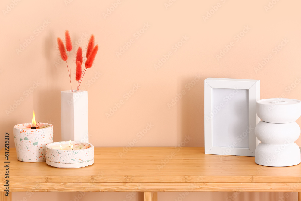 Holders with burning candles and blank frame on table near beige wall in room