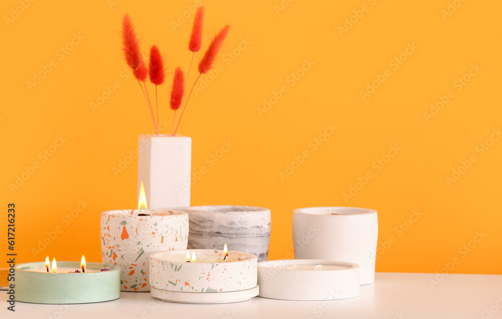 Holders with burning candles and lagurus on table near orange wall in room