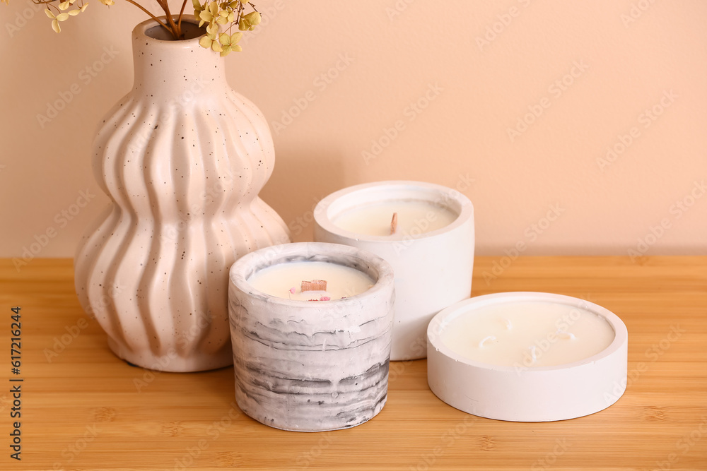 Holders with candles and flowers on table near beige wall in room, closeup