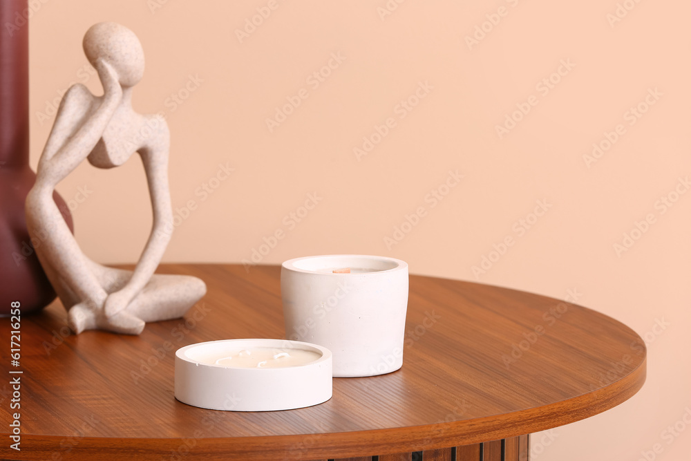 Holders with candles and decor on table near beige wall in room