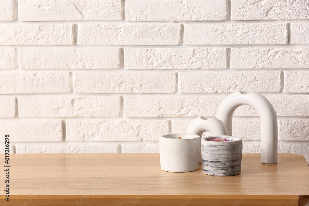 Holders with candles and decor on table near light brick wall in room