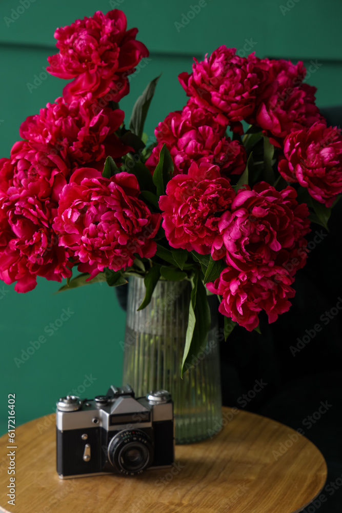 Vase of red peonies with camera on coffee table near green wall