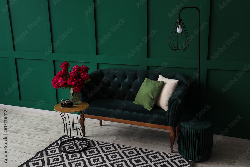 Vase of red peonies with coffee table, couch and floor lamp near green wall