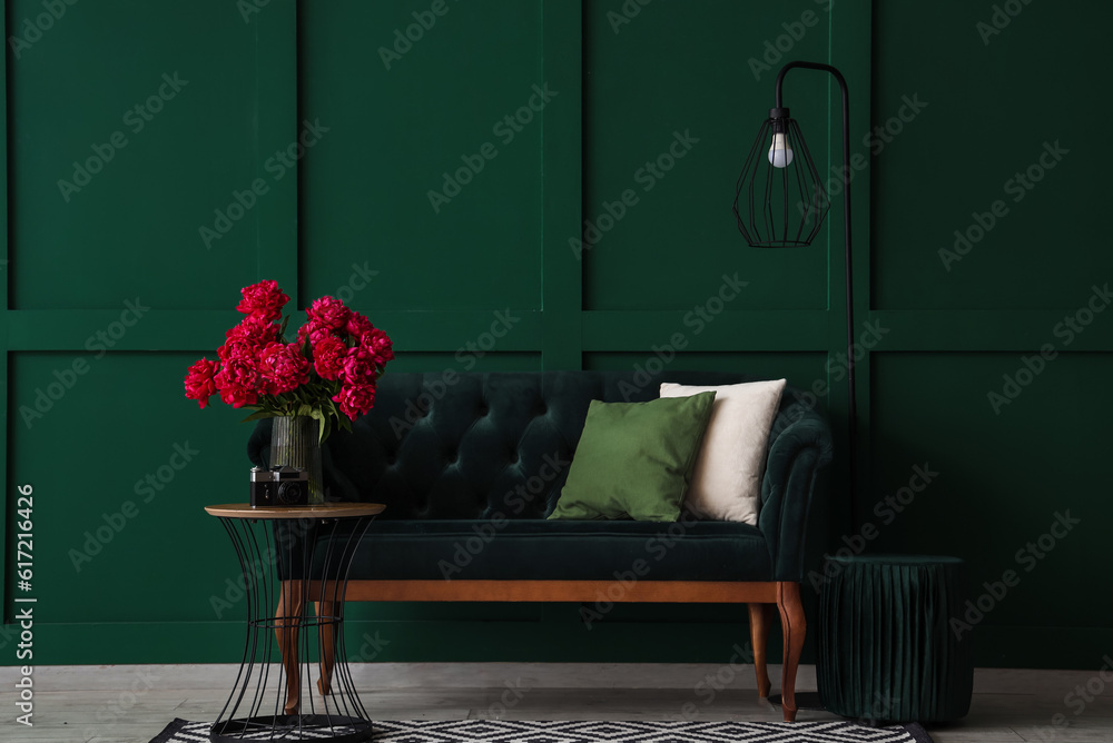 Vase of red peonies with coffee table, couch and floor lamp near green wall