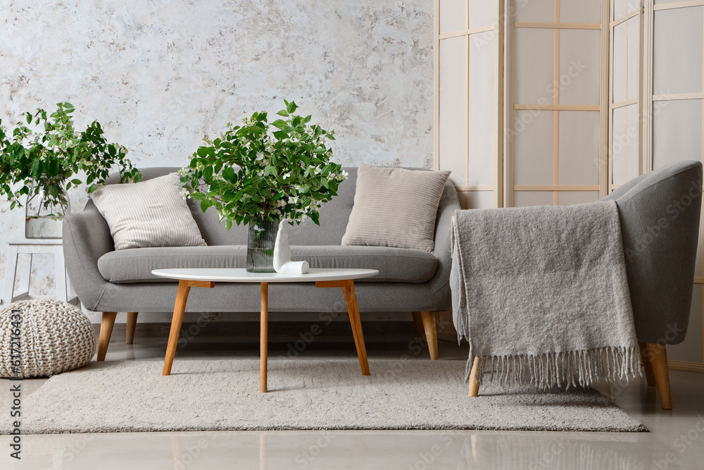 Interior of living room with cozy grey sofa and blooming jasmine flowers on coffee table