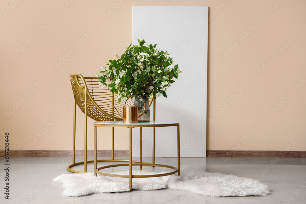 Vase with blooming jasmine flowers on coffee table and stylish armchair near beige wall