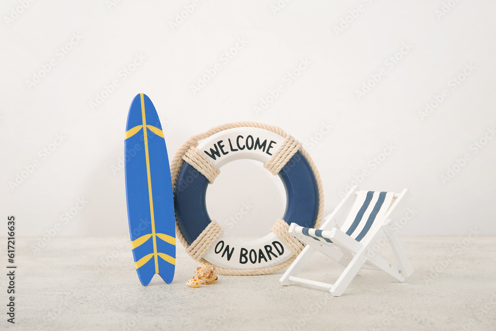 Creative composition with miniature surfboard, deckchair and life buoy on white table