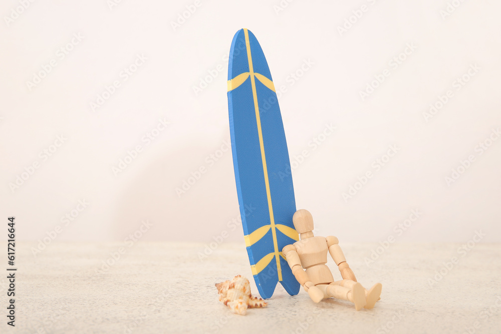 Creative composition with miniature surfboard, wooden mannequin and seashells on white table