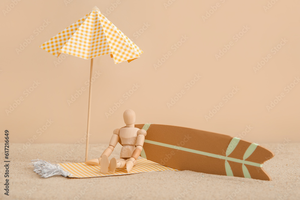 Creative composition with miniature surfboard, umbrella and wooden mannequin on sand against beige b