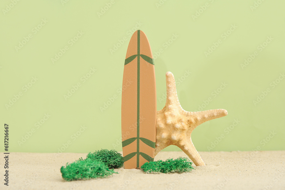 Mini surfboard with starfish and moss on sand against olive background