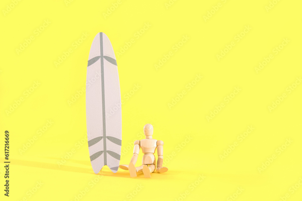 Creative composition with miniature surfboard and wooden mannequin on yellow background