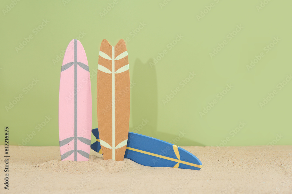 Different colorful mini surfboards on sand against olive background