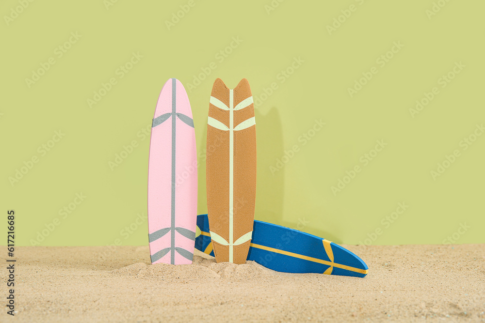 Different colorful mini surfboards on sand against olive background