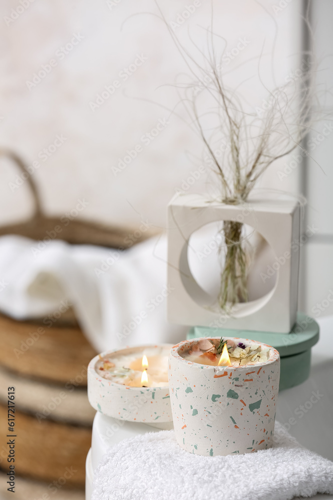 Holders with burning candles and towel on bathtub in bathroom, closeup