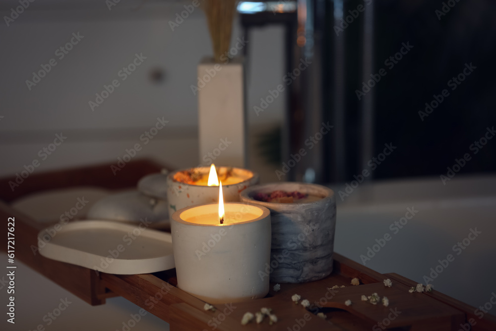 Holders with burning candles on wooden stand in bathroom, closeup