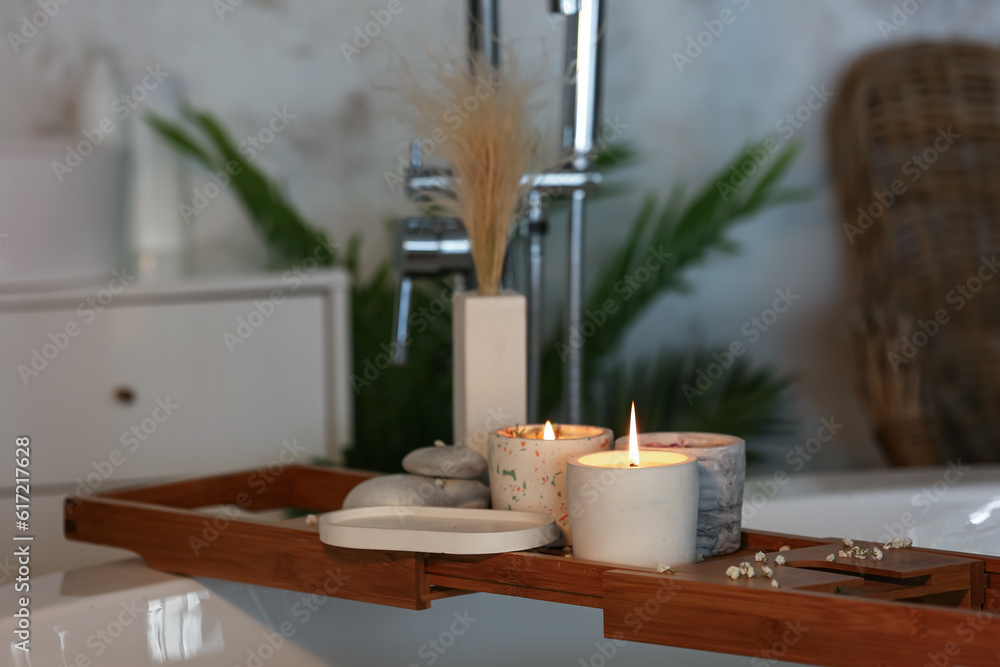 Holders with burning candles on wooden stand in bathroom, closeup