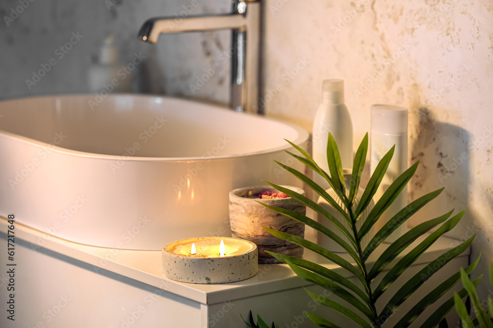 Holder with burning candle and sink on table in bathroom, closeup