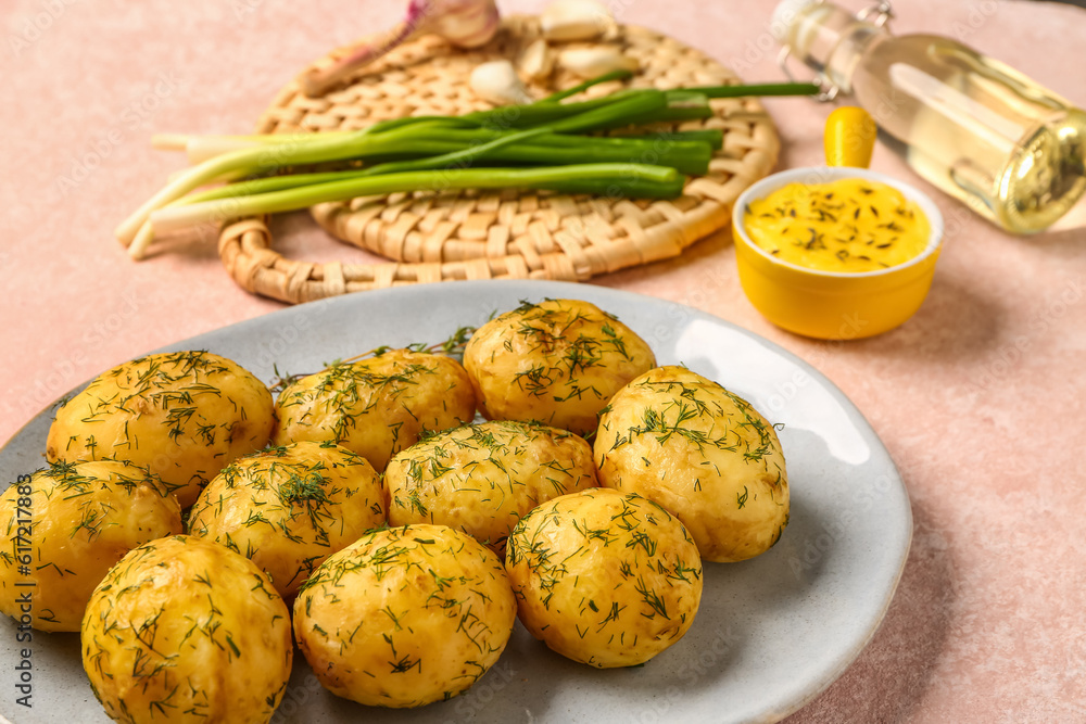 Plate of boiled baby potatoes with dill and green onion on pink background