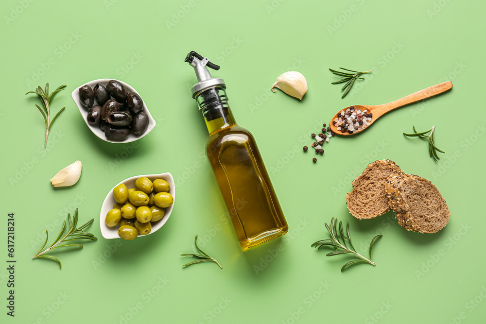 Bowls with ripe olives, bread and bottle of oil on green background