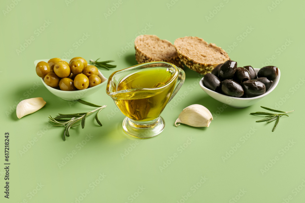 Bowls with ripe olives and gravy boat of oil on green background