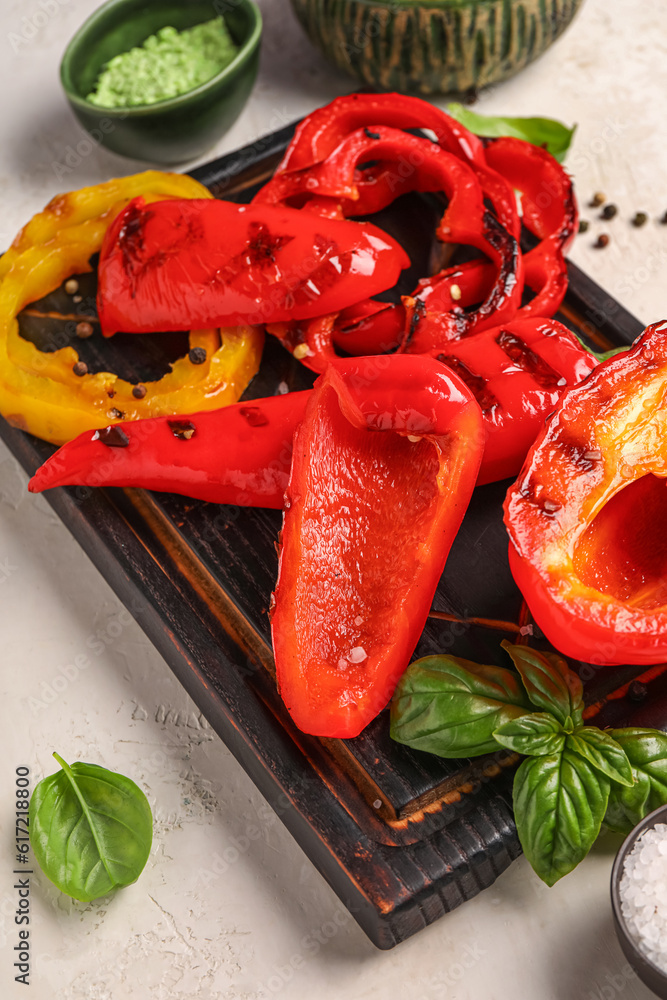 Wooden board with tasty grilled peppers on light background