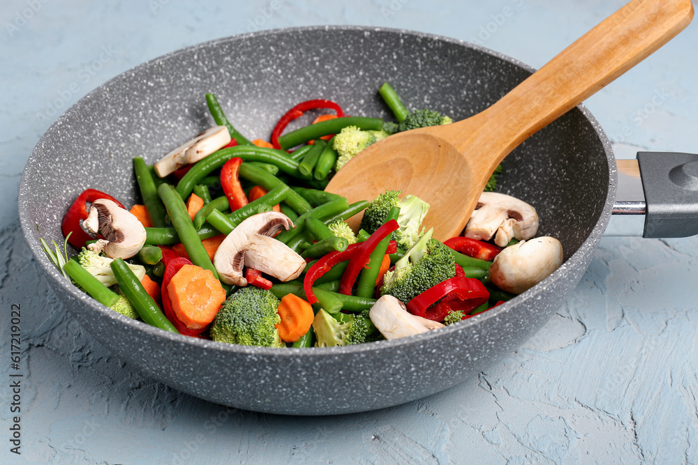 Frying pan with fresh vegetables on grey background