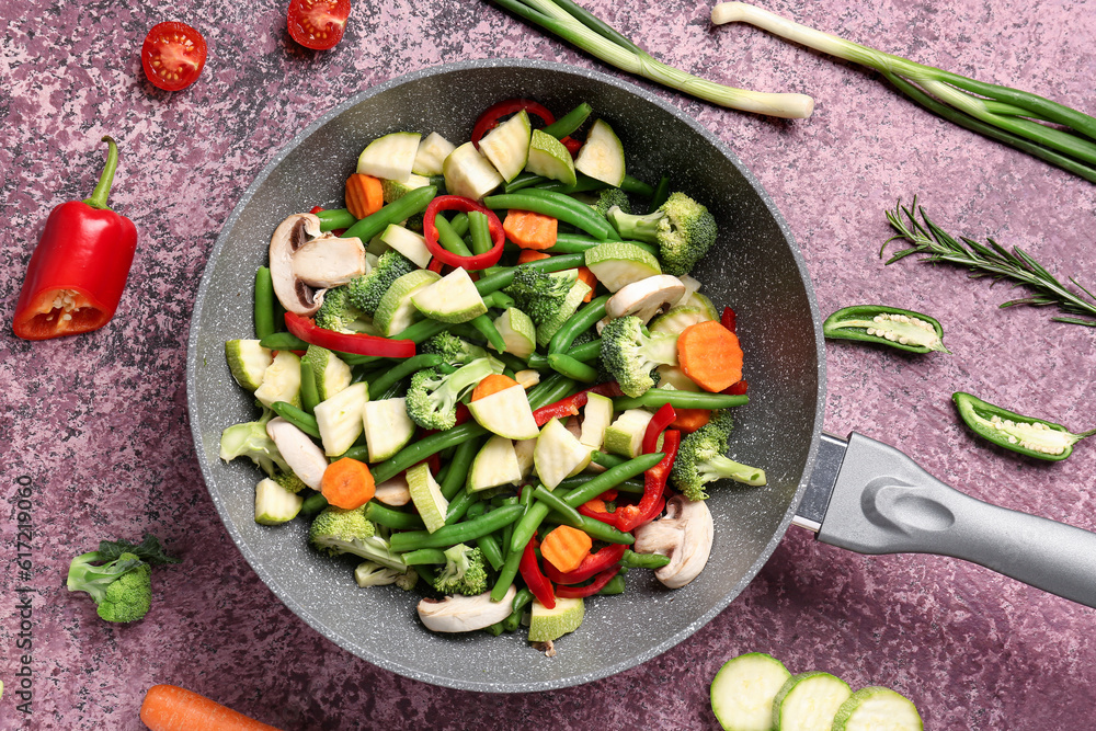 Frying pan with fresh vegetables on purple background