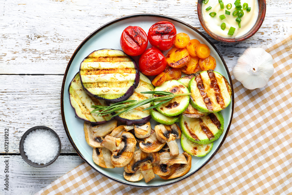 Plate with grilled vegetables and sour cream on white wooden background