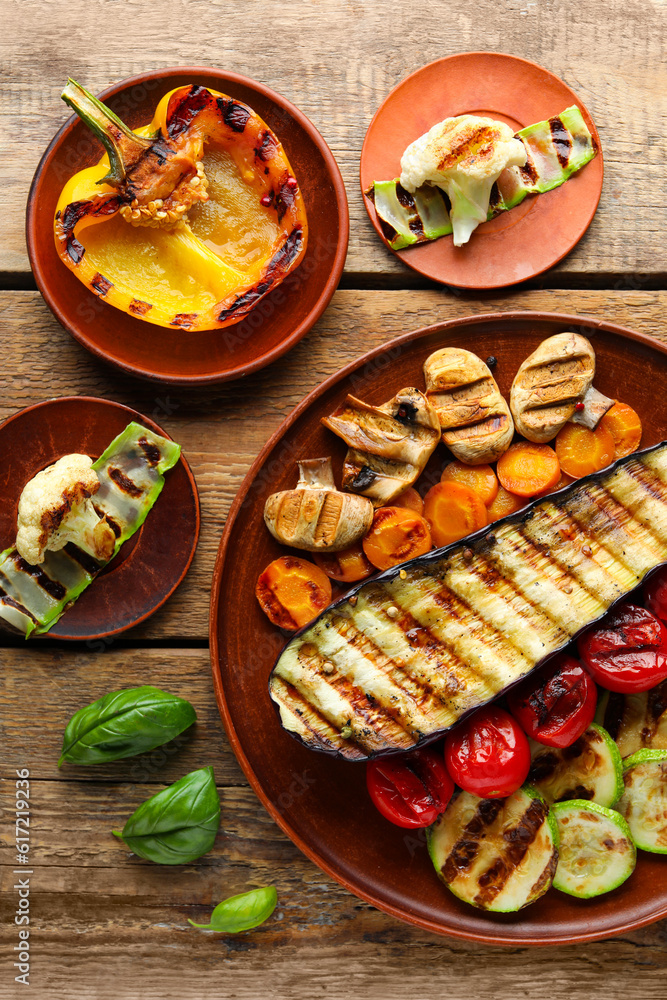 Plates with grilled vegetables and basil on wooden background