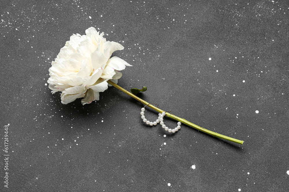 Beautiful female earrings and peony flower on dark background