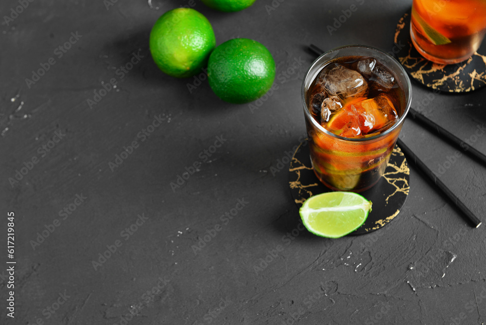 Glasses of cold Cuba Libre cocktail and limes on grey table