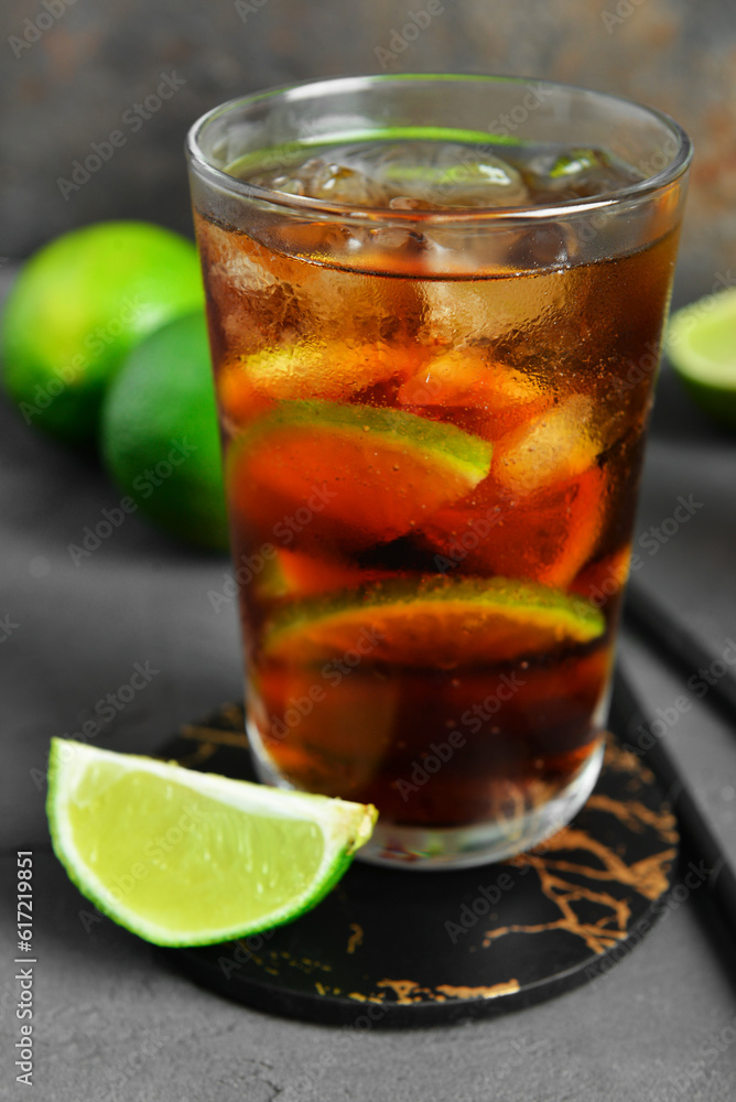 Glass of cold Cuba Libre cocktail and limes on grey table