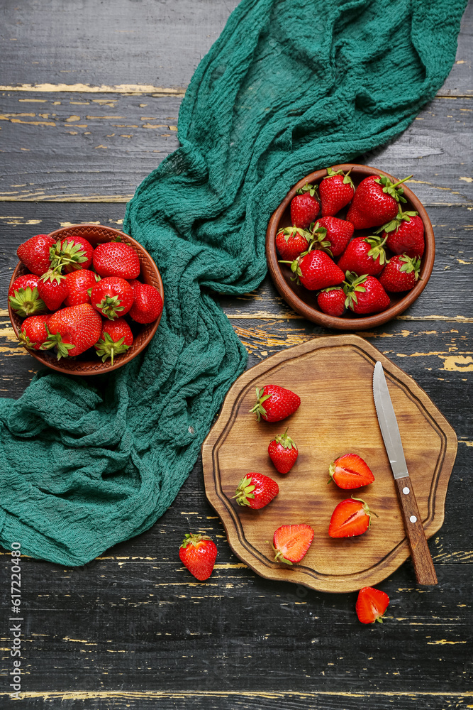 Bowl and plate with fresh strawberries on black wooden background