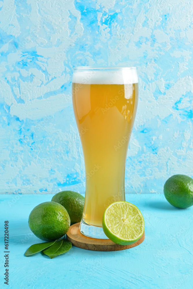 Glass of cold beer with lime on blue background