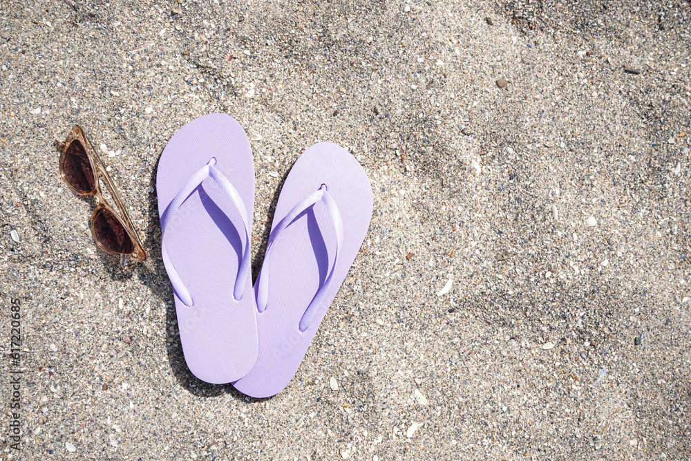 Lilac flip-flops with sunglasses on sand beach background