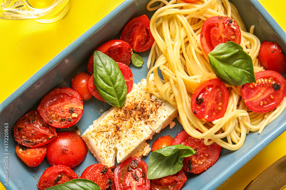 Baking dish of tasty pasta with tomatoes and feta cheese on yellow background